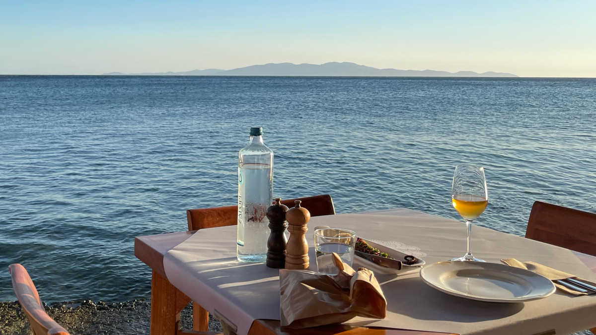 Tinos travel guide dining setting with ocean view, featuring drinks and a table ready for a meal.