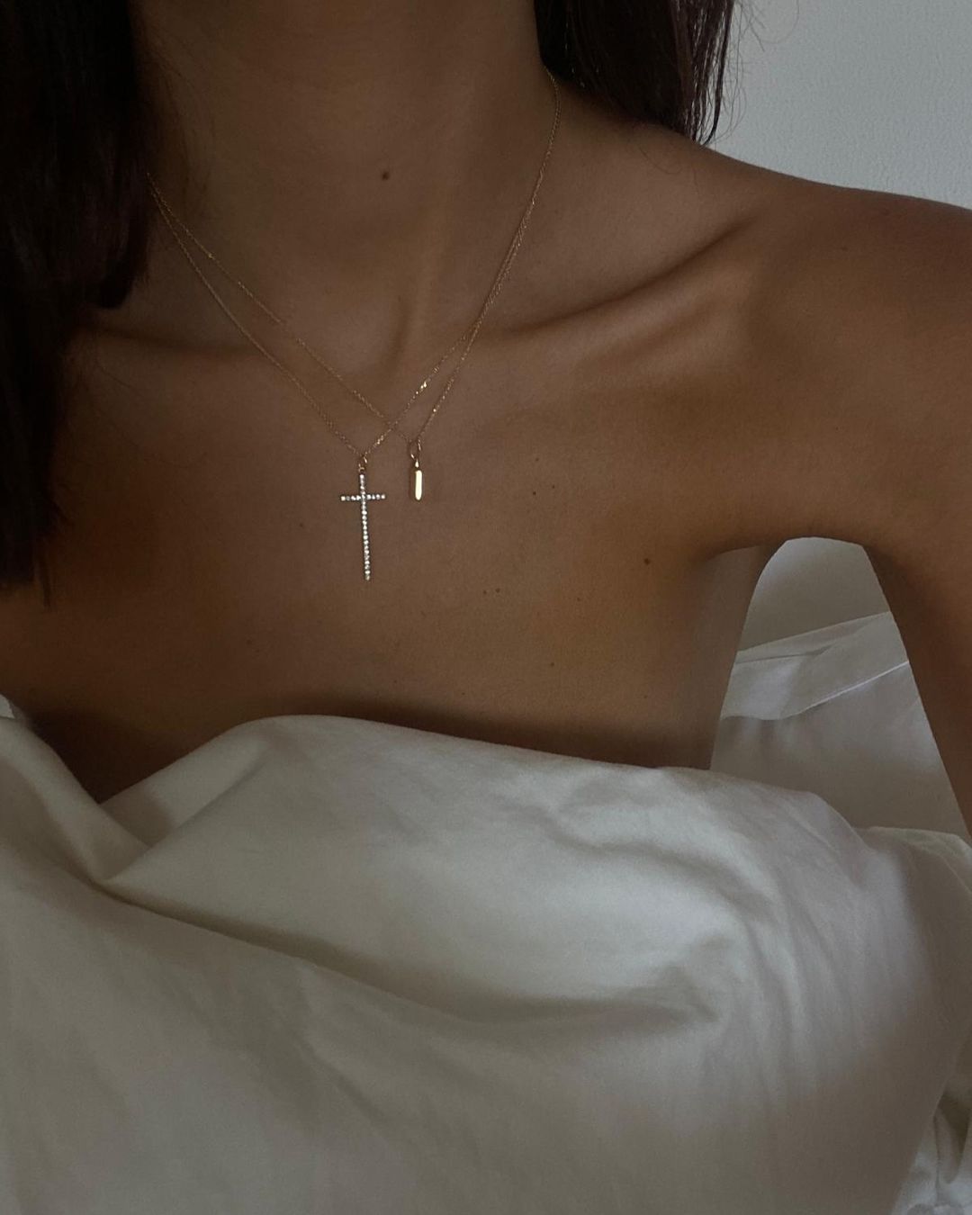 Minimal gold jewelry elegance featuring layered necklaces with a cross and a pendant.