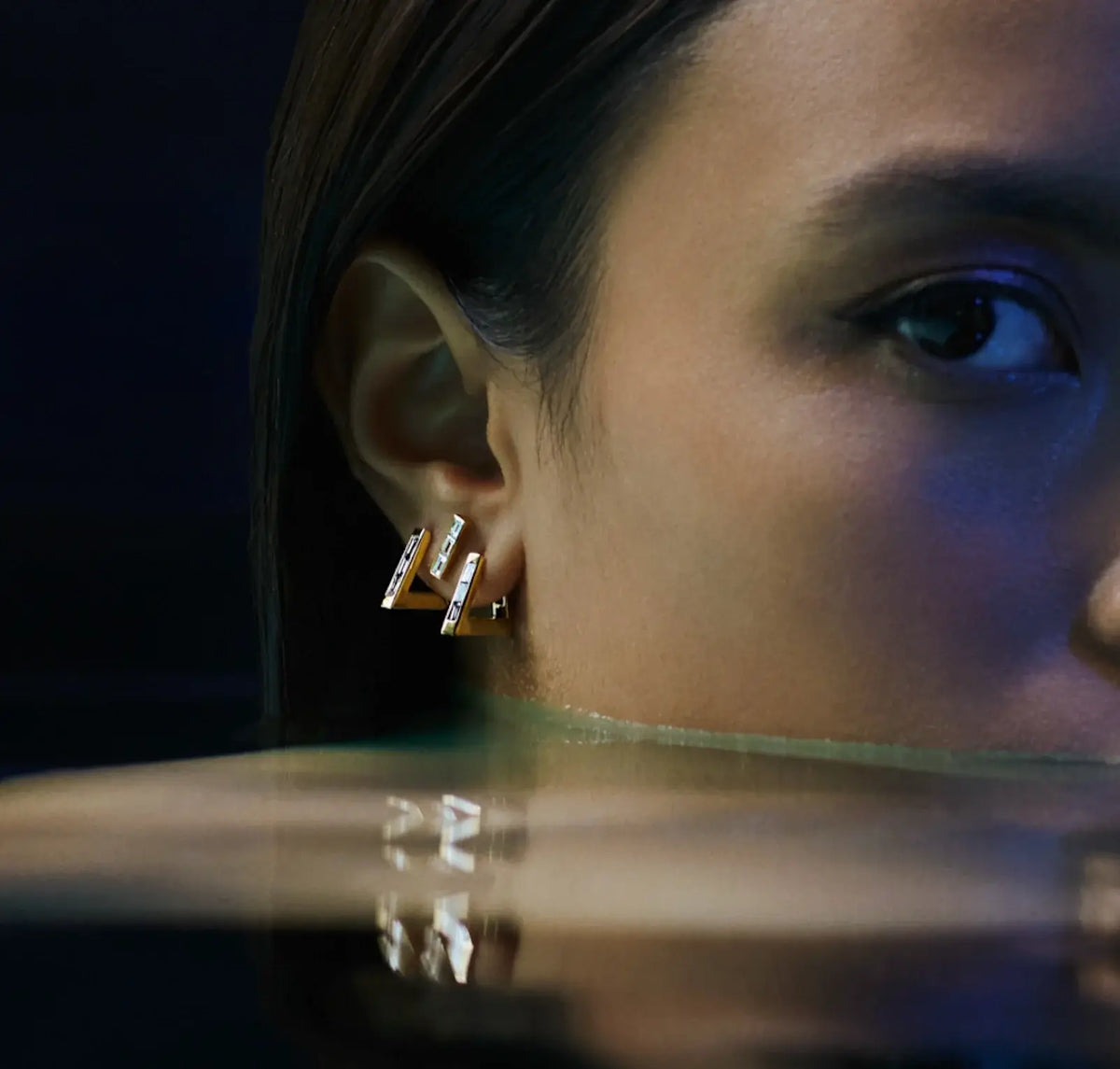 topaz triangle hoop earring showcased on model's ear, reflecting elegance in a serene aquatic setting