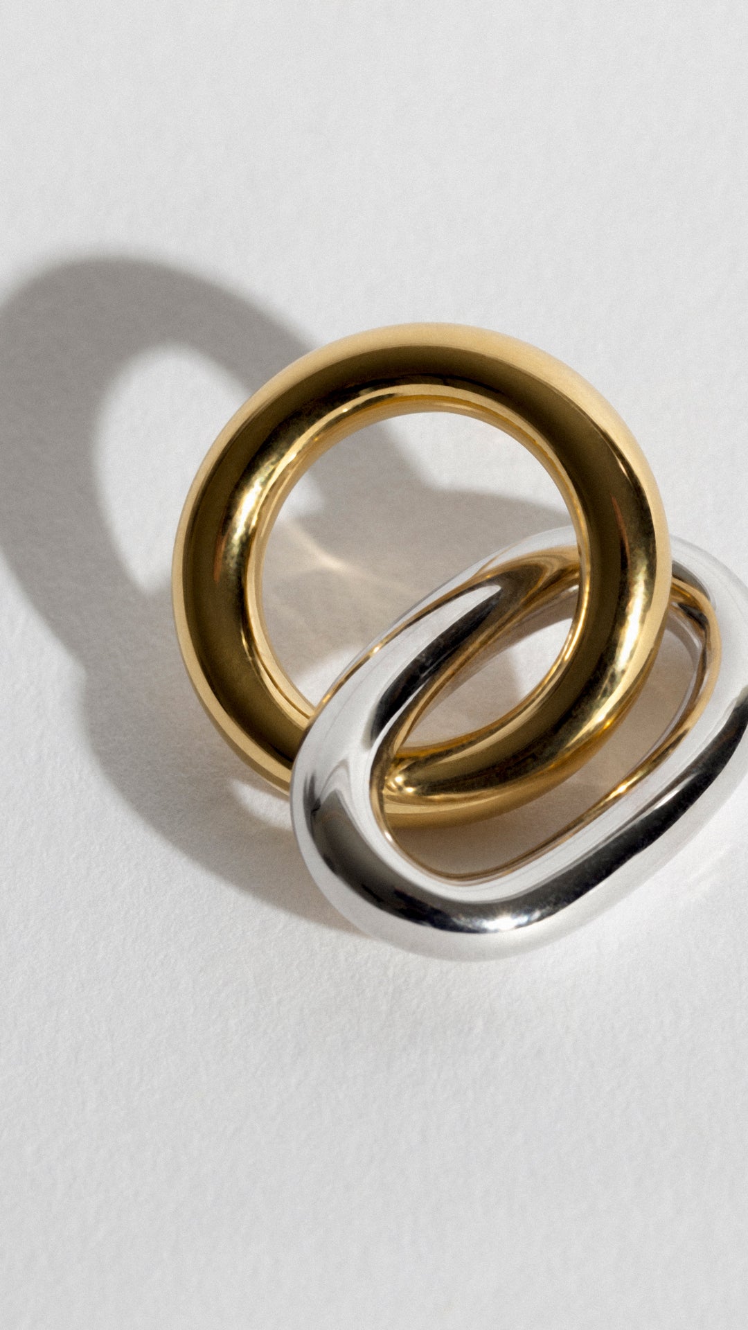 Elegant wedding jewelry for guests featuring intertwined gold and silver rings on a light background.