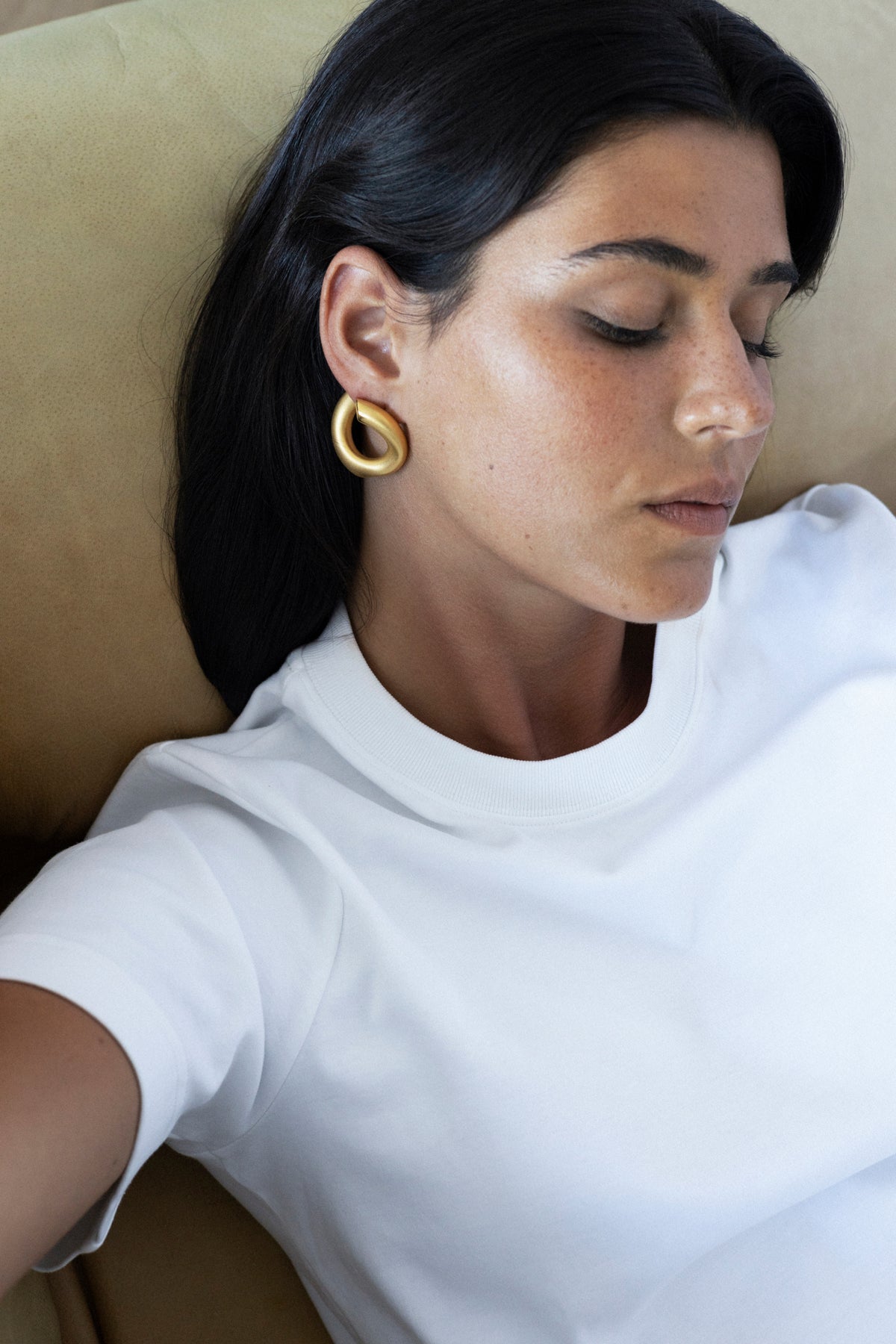 Close-up of a woman wearing large gold earrings, in a casual white t-shirt. Jewelry inspired by women.