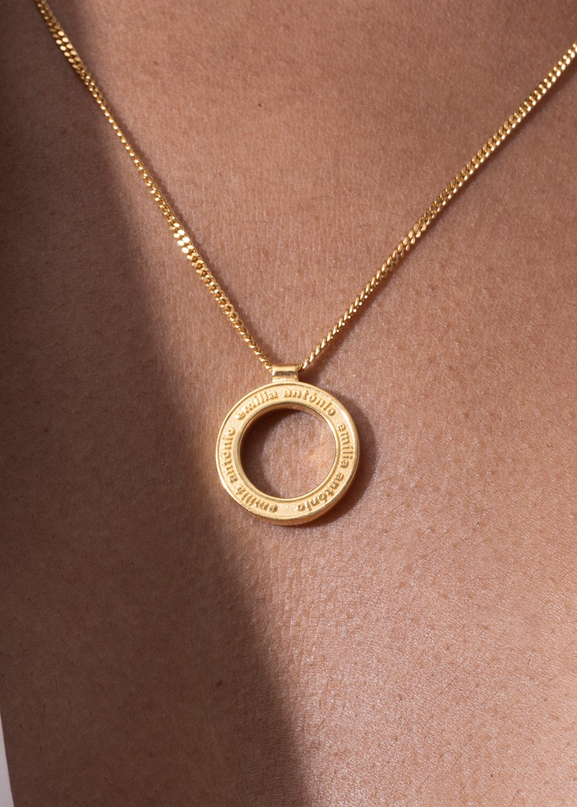 Personalized engravable necklace featuring a gold disc pendant with engraved details, displayed on a model's neck.