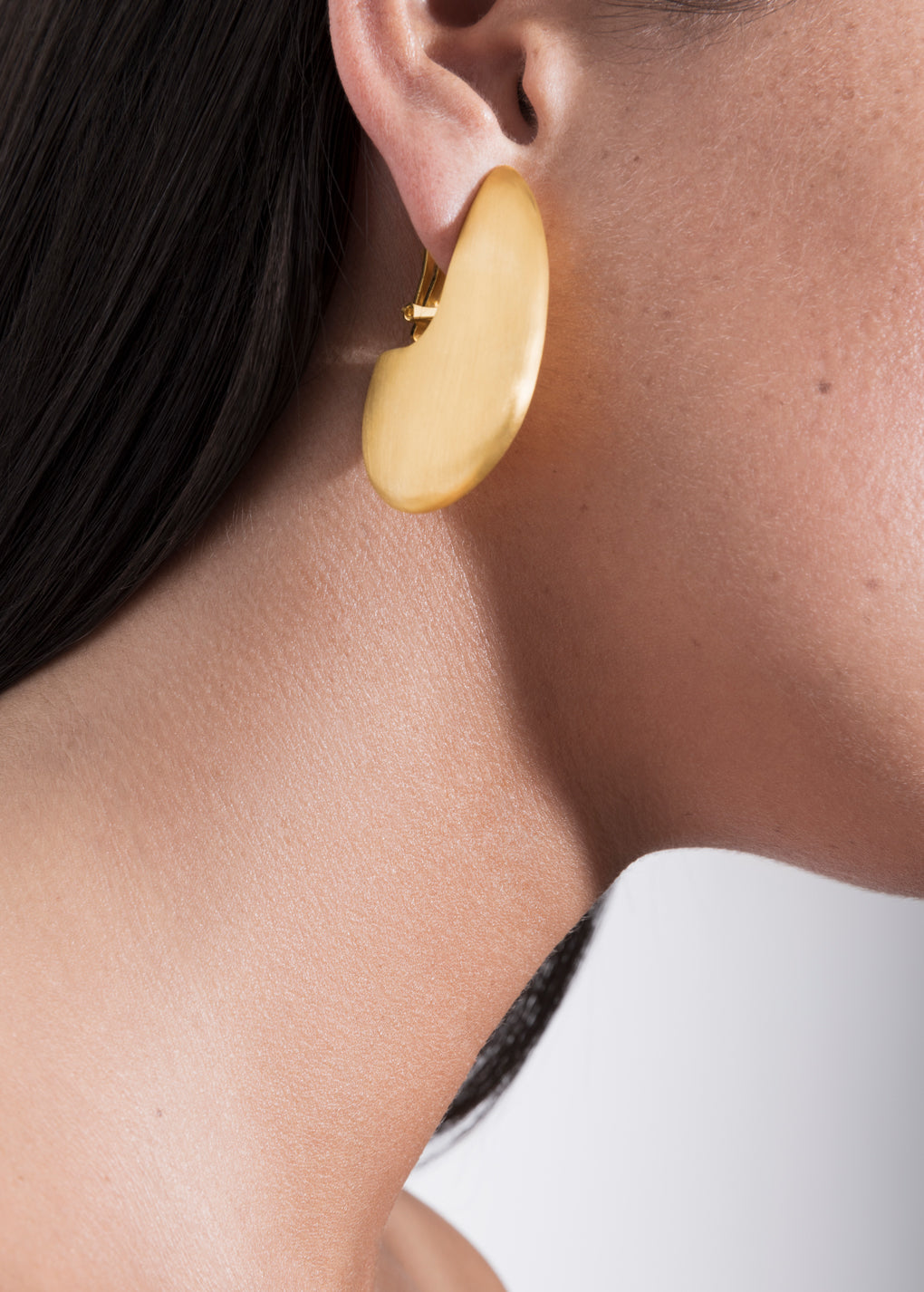 Pam Family sculptural earrings shown on model's ear, featuring bold geometric silhouette in gold finish.