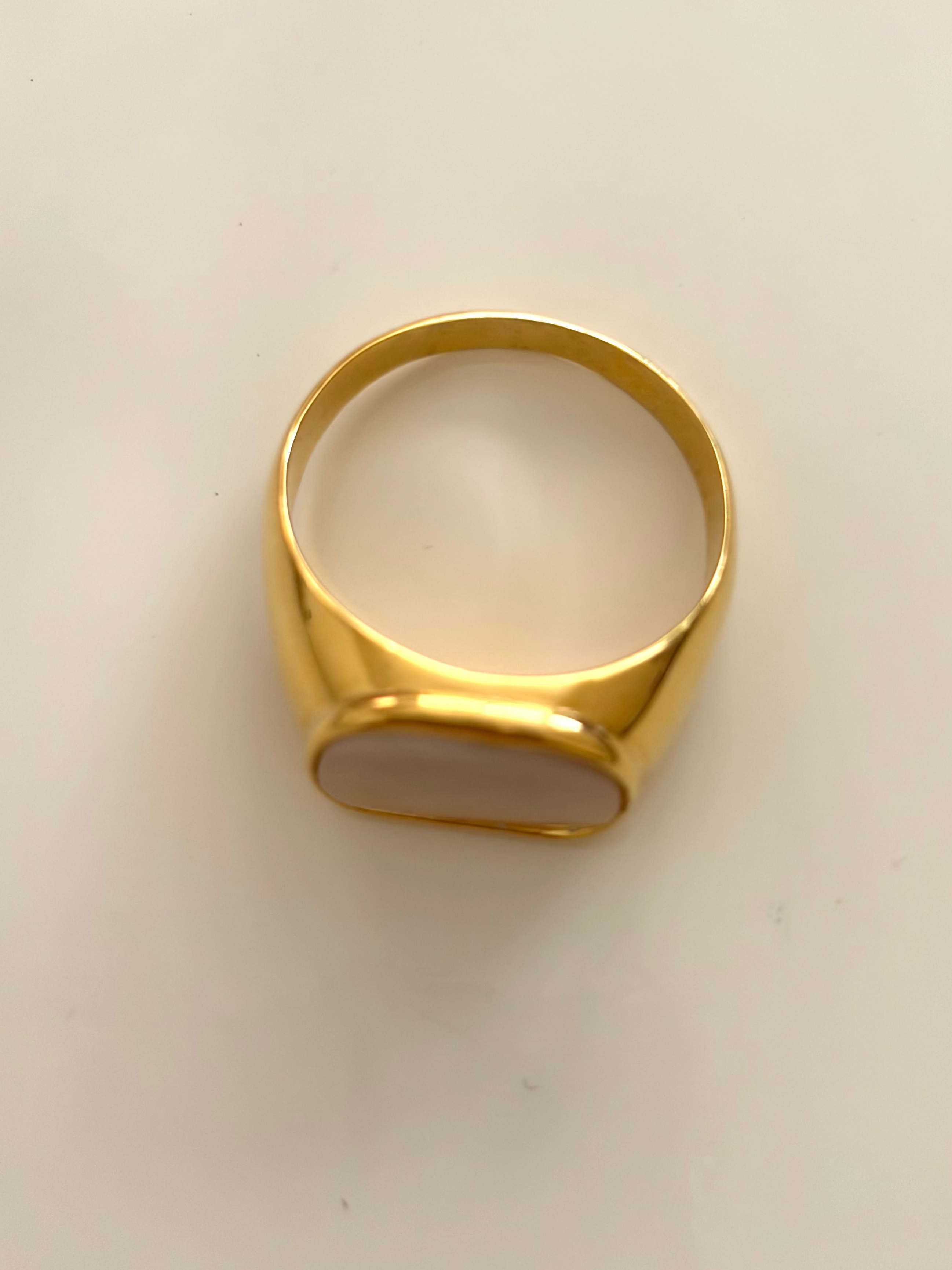 A gold signet ring with a smooth, polished oval face, photographed from above on a plain off-white background.