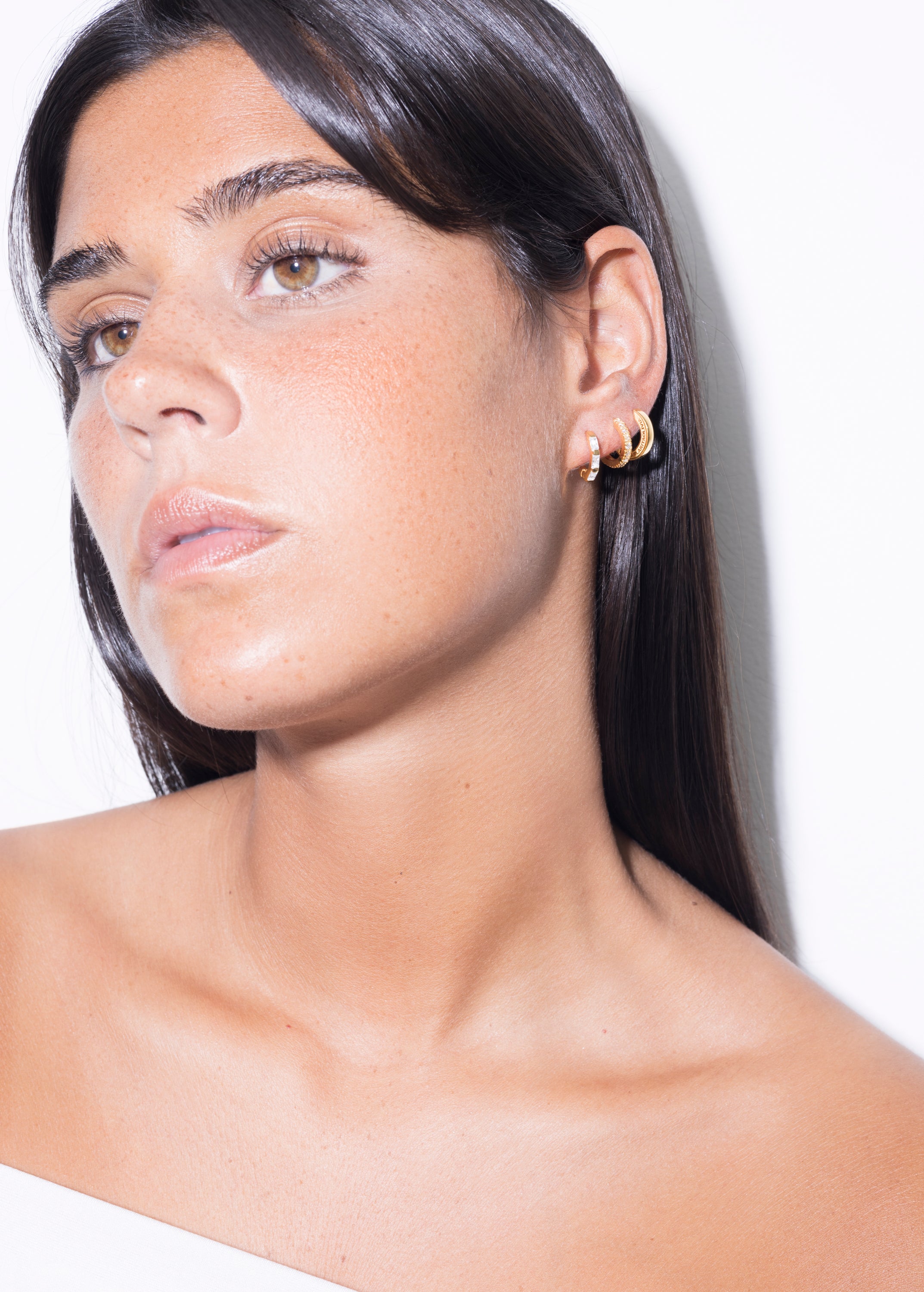 model wearing amina huggies white, norma earrings white and  jodie huggies in gold