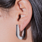 Close-up of an ear wearing a silver hoop earring with dark hair.