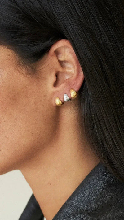 Tilly huggie earrings silver gold worn on a woman's ear, showcasing gold and silver plating, elegant and stylish.