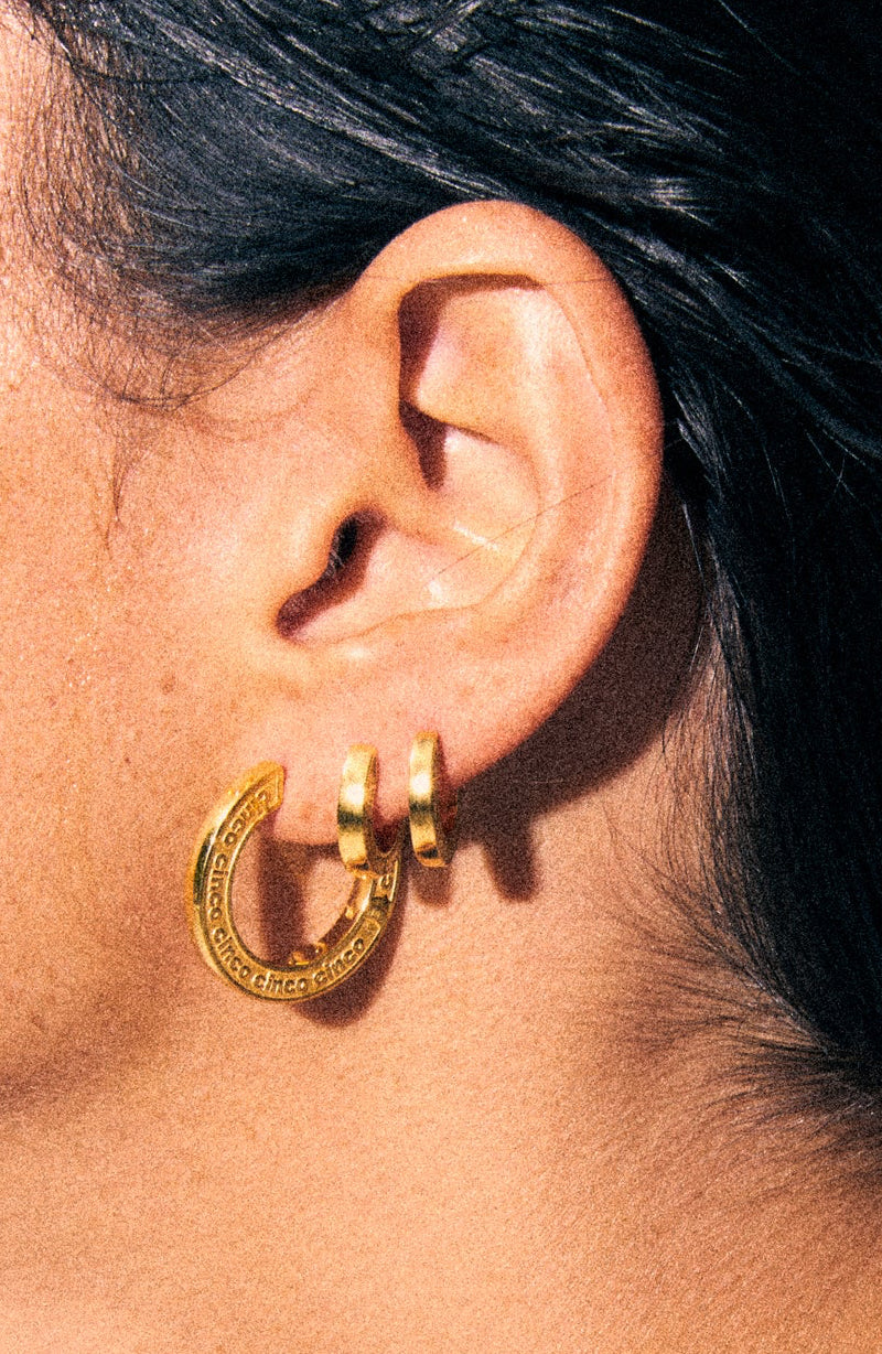 Close-up of a person wearing a gold hoop earring with a neutral background