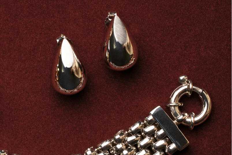 Gold teardrop-shaped earrings and bracelet on a maroon background